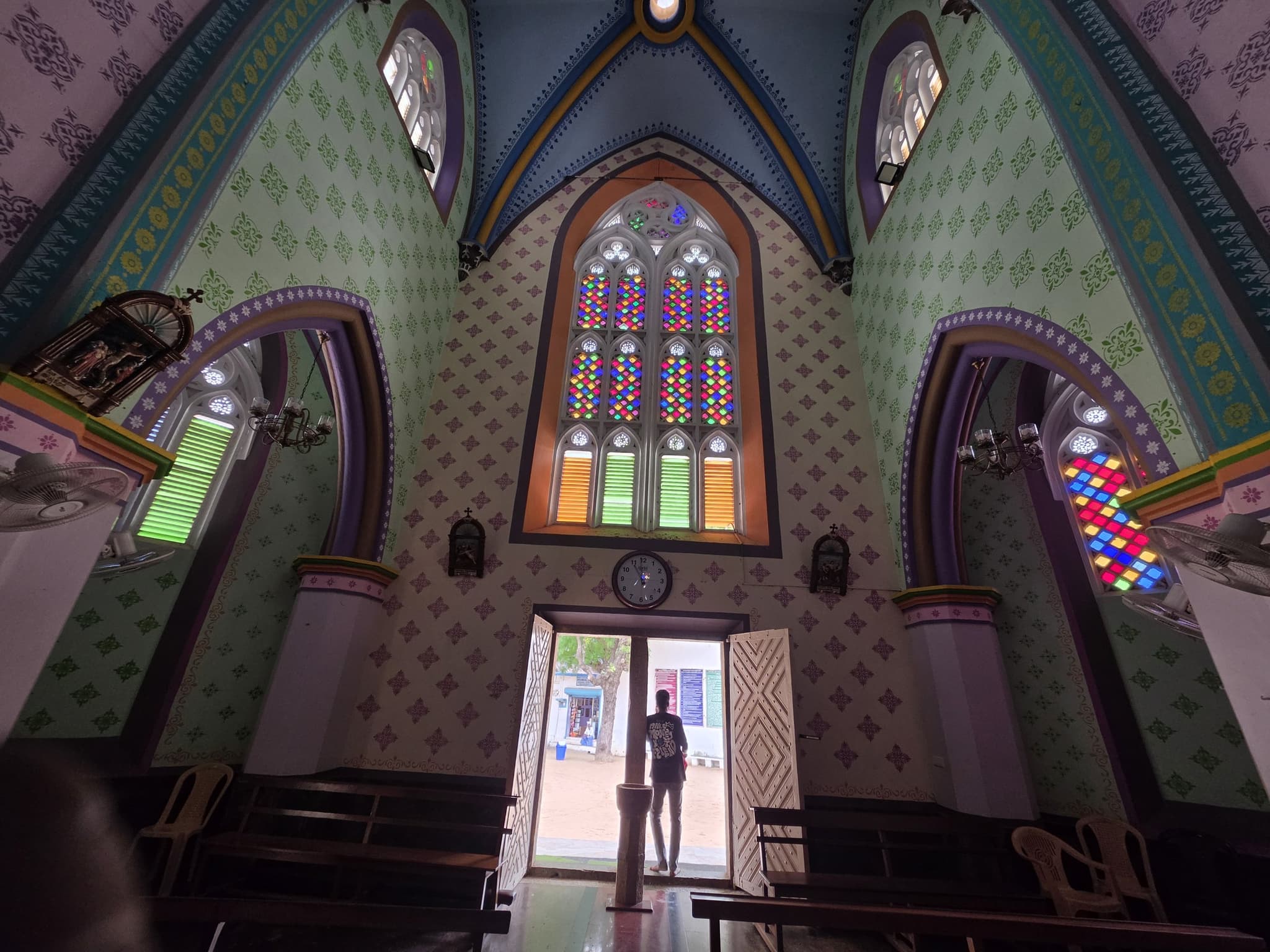 The interior of the church looking back down the nave to the west door, the painted rib vault overhead and a figure standing in the light of the open doorway