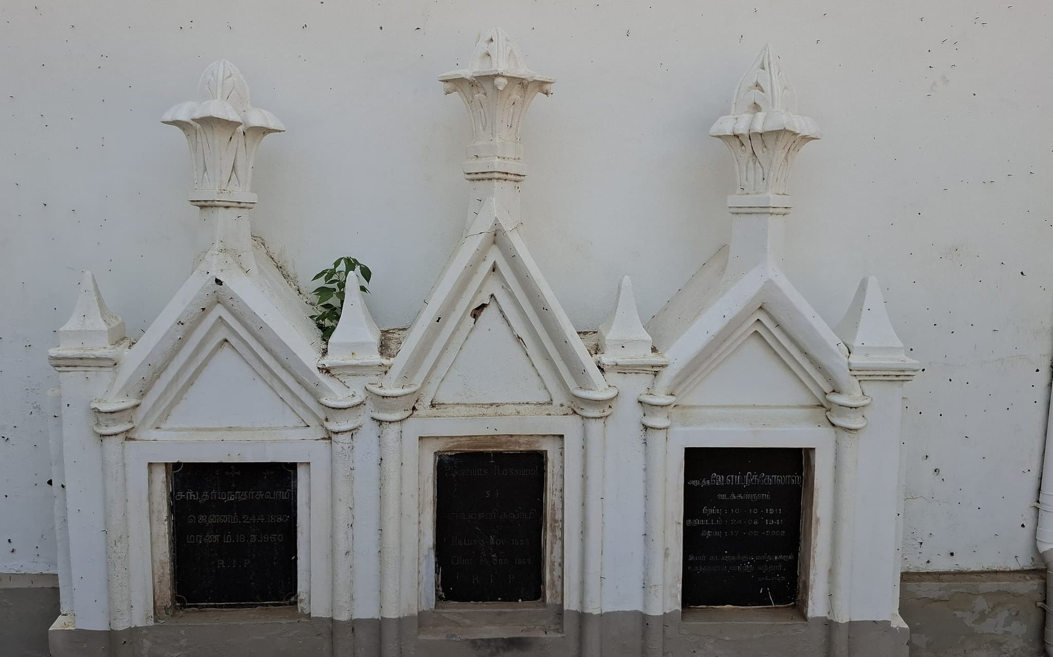 Three whitewashed Gothic tomb monuments in a row against the church wall, each with a black inscribed plaque: Fr Dharmanathar, Fr Eugène Rossignol S.J., and Fr J. M. Nicholas.